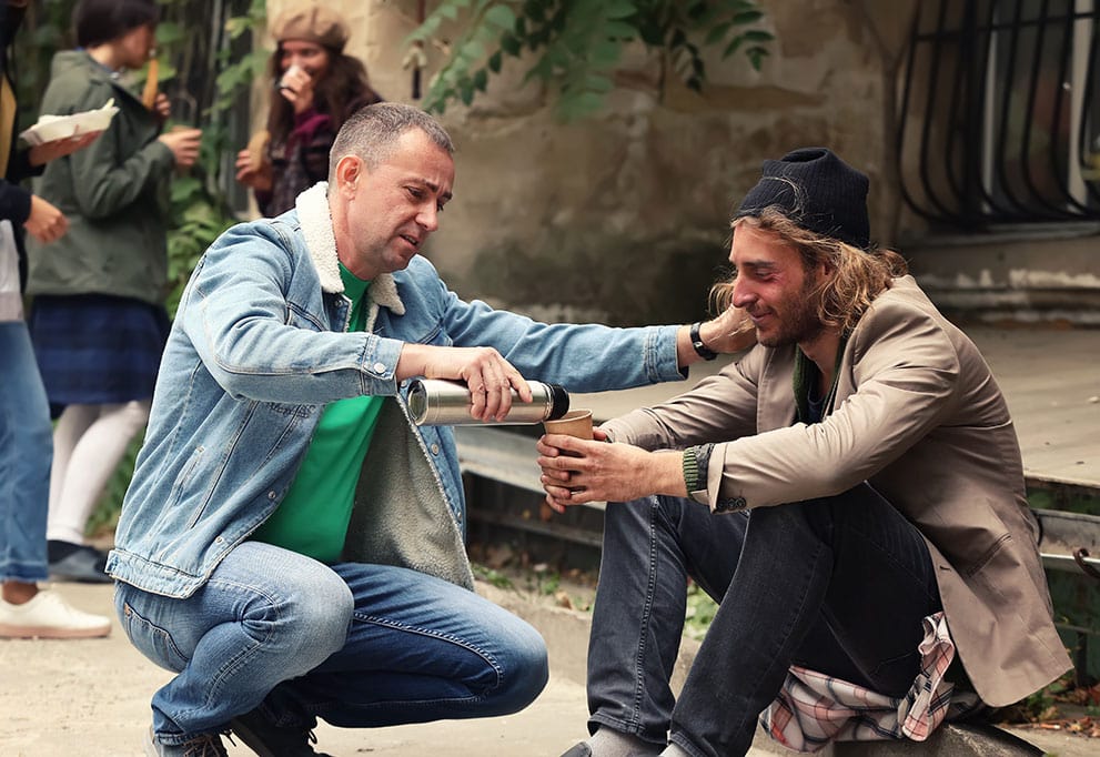 Two men sharing a meal outdoors in a friendly gesture.